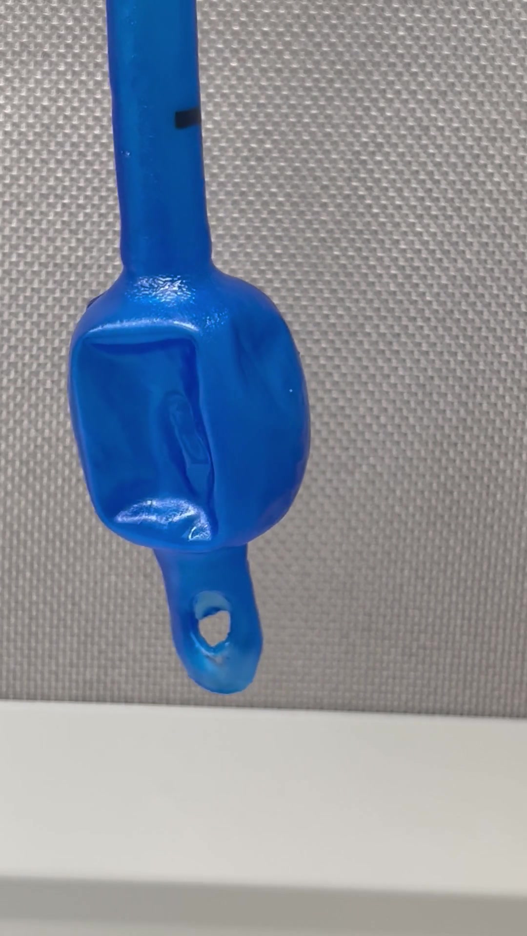 The cuff of a coated endotracheal tube, an even blue, hanging against a gray wall.